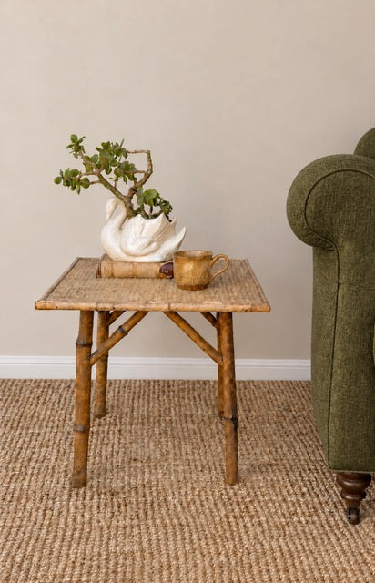 Vintage tiger bamboo side table styled beside an olive green armchair 