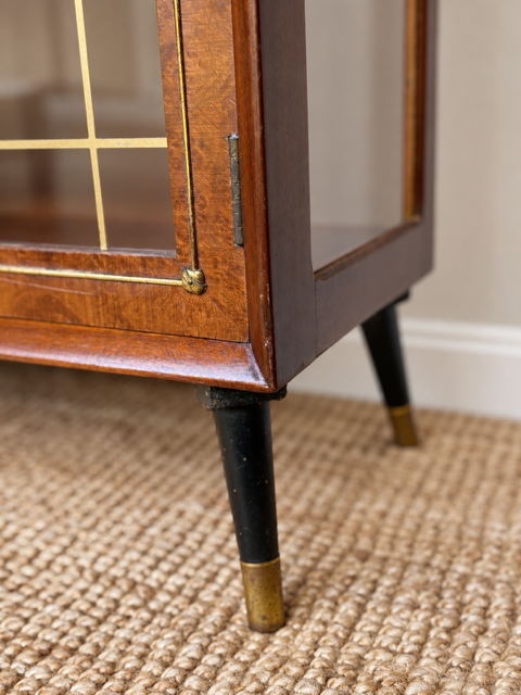 Close-up of the vintage display cabinet's wooden corner and black tapered legs with brass feet, standing on natural sisal