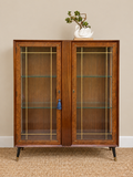 Vintage wooden display cabinet with glazed doors, geometric detailing, glass shelves and black legs with brass feet