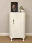 Vintage cream Art Deco storage cabinet with curved front and geometric door detail, styled with vintage artwork and flowers